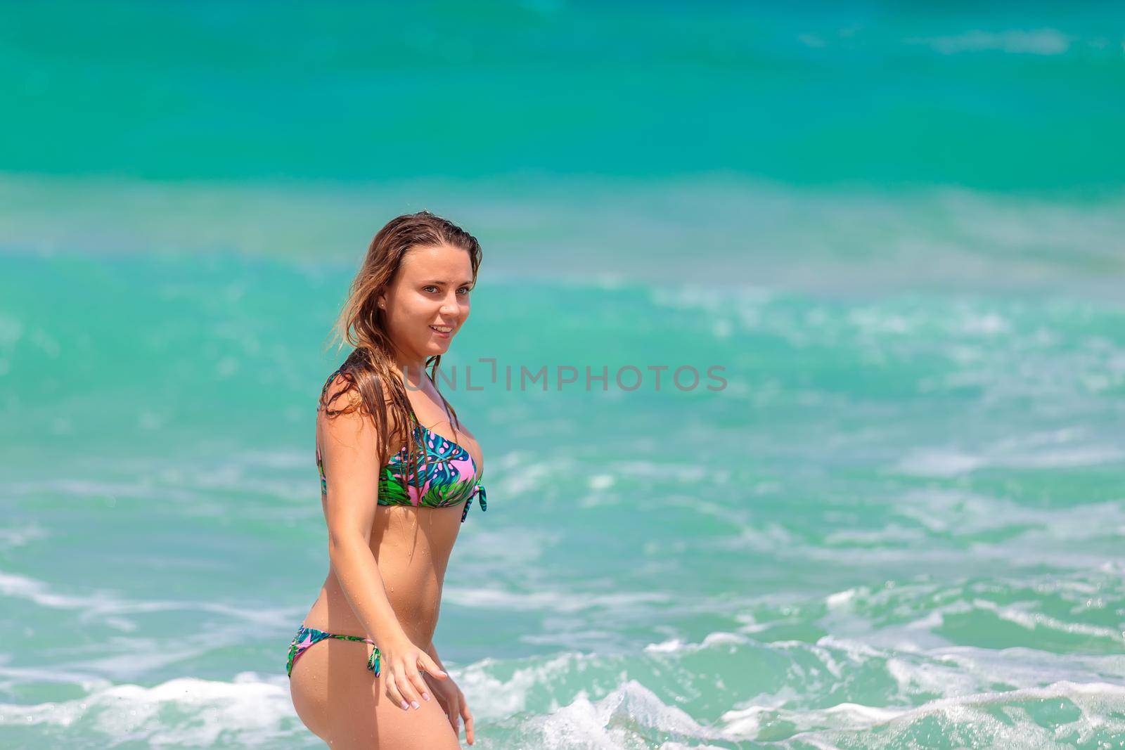 Young beautiful girl enjoys the sea and the waves, laughing raising her hands up in a black fashionable swimsuit.