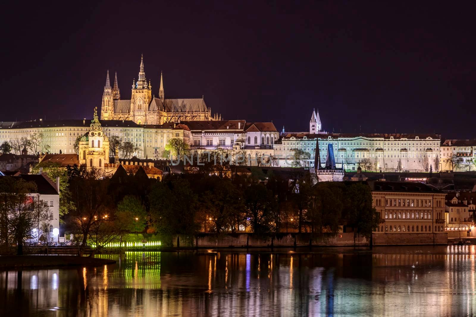 Charles Bridge in Prague in the evening with colorful lights from lanterns. In the river the reflection of the evening illuminations.