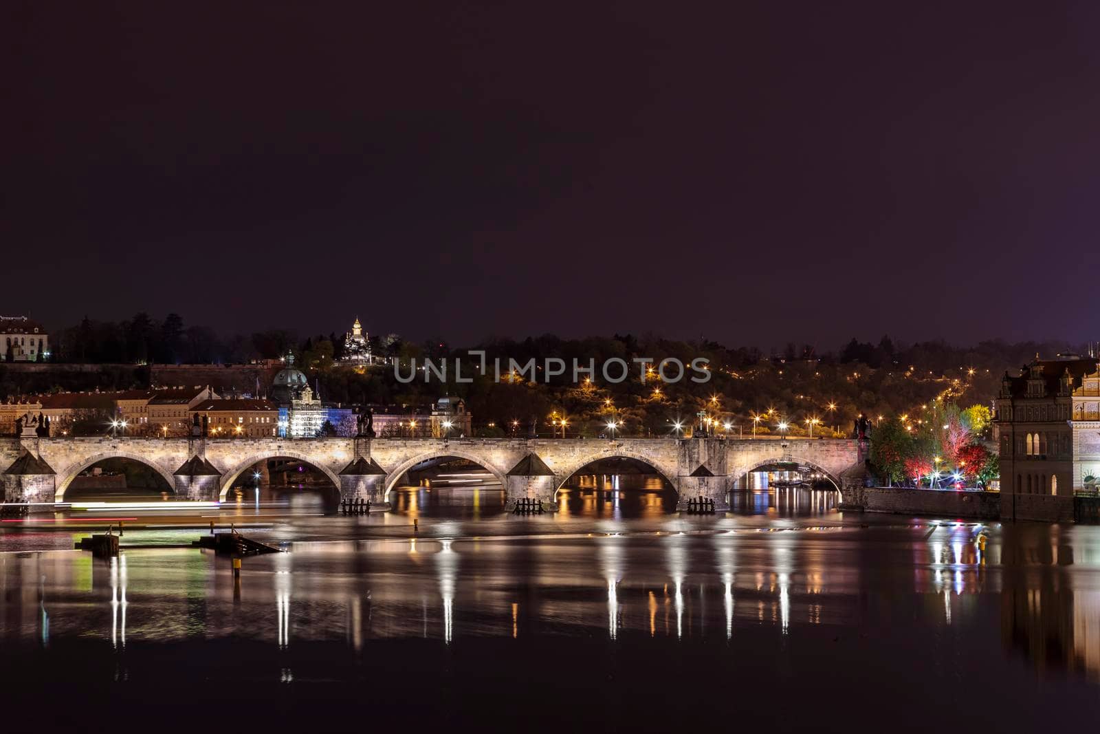 Charles Bridge in Prague in the evening with colorful lights from lanterns. In the river the reflection of the evening illuminations.
