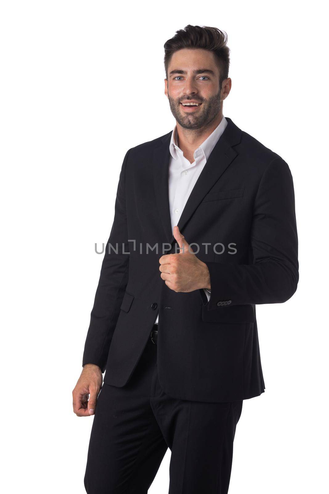 Portrait of young handsome business man in black suit smiling and showing thumbs up studio isolated on white background