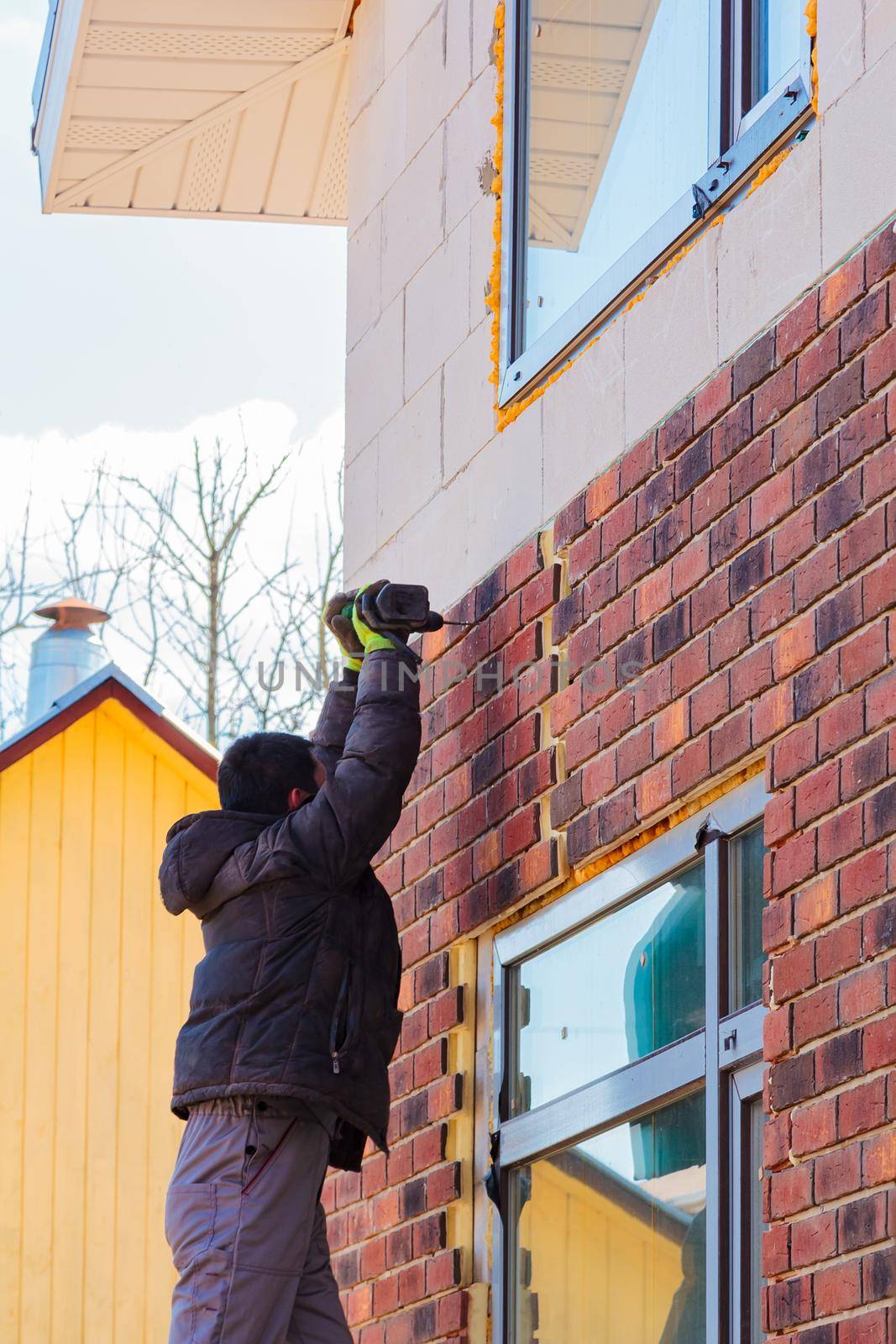A man works with a drill, attaches thermal panels made of clinker to the facade of the house. Clinker bricks and tiles in brown color