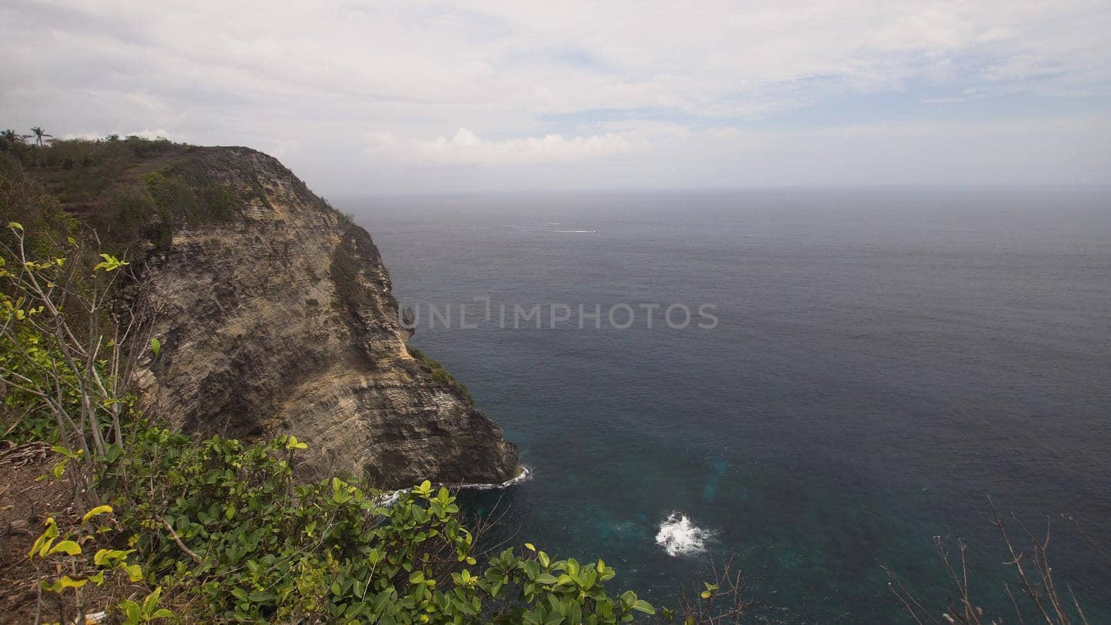 Cliff with waves crashing against rocky shore, Nusa Penida, Indonesia. Rocky coast and ocean with waves and rocky cliff. Travel concept.