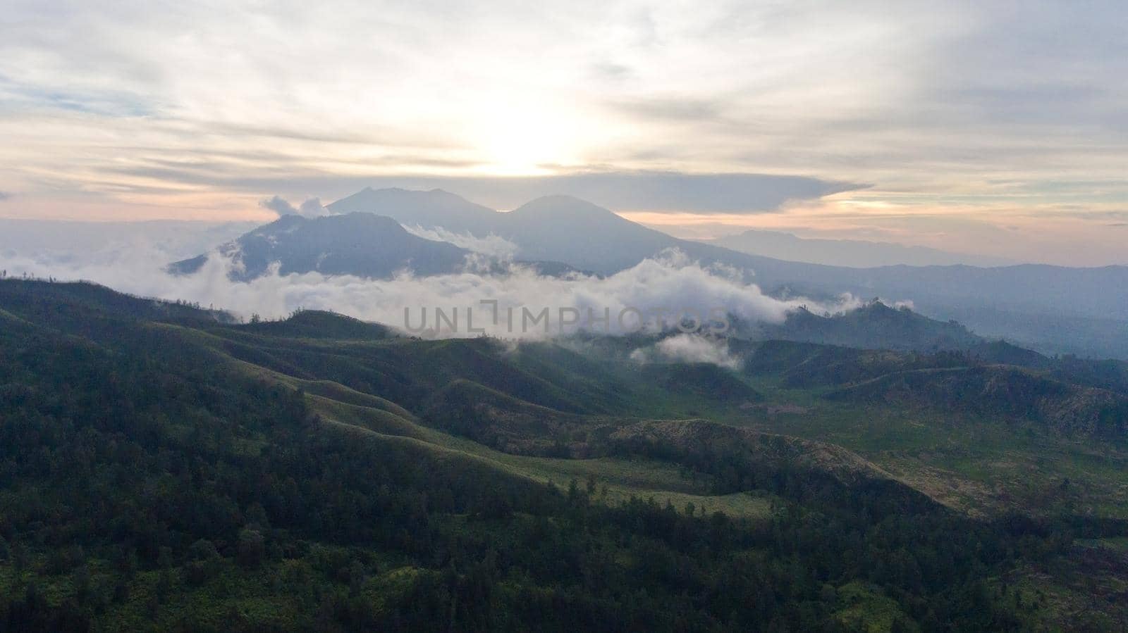 Aerial view of forest, mountains with fog, clouds at sunset on Bali,Indonesia. Tropical rainforest, trees, jungle in mountains. Fog over the jungle. Travel concept.
