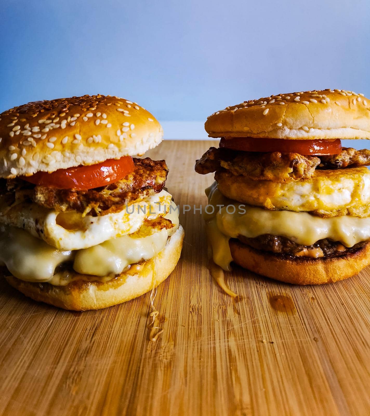 Two burgers with tomato bacon grilled cheese and beef on wooden board by Wierzchu