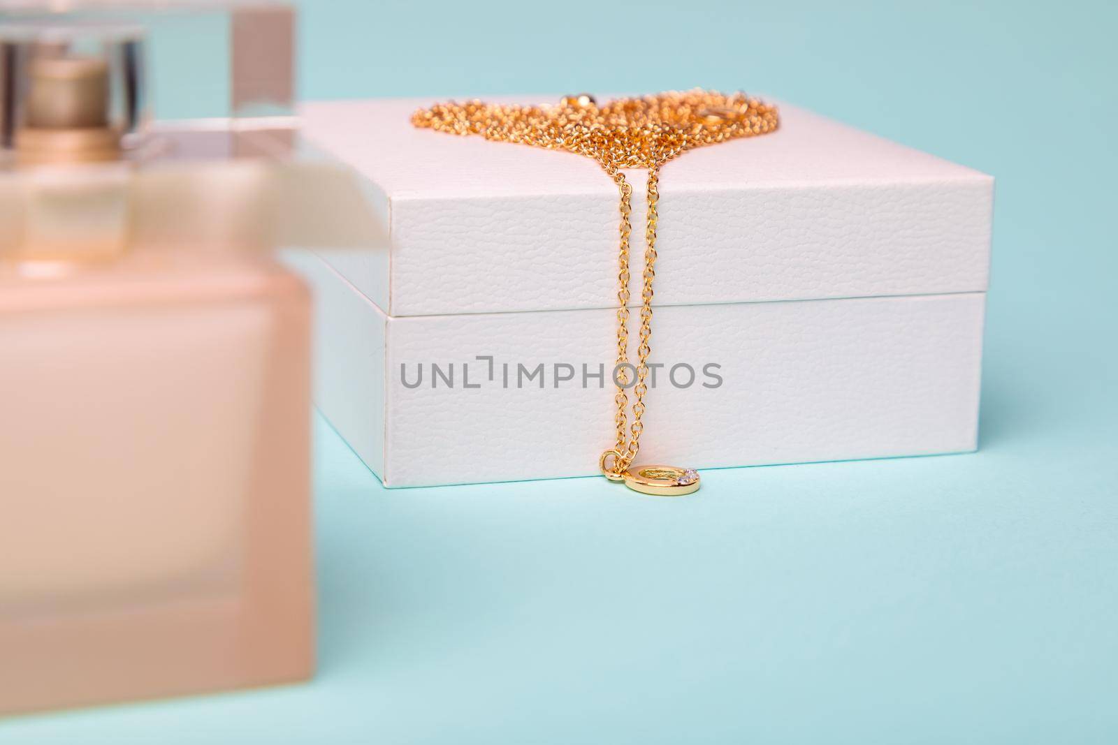 A gift for Valentine's Day. Perfume and a box with a gold chain on a blue background. Chain in the shape of a heart.