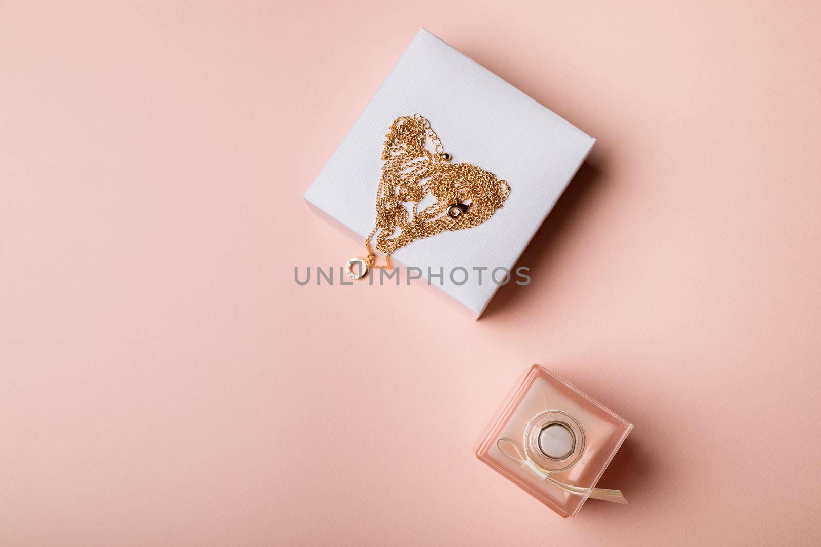 A gift for Valentine's Day. Perfume and a box with a gold chain on a pink background.