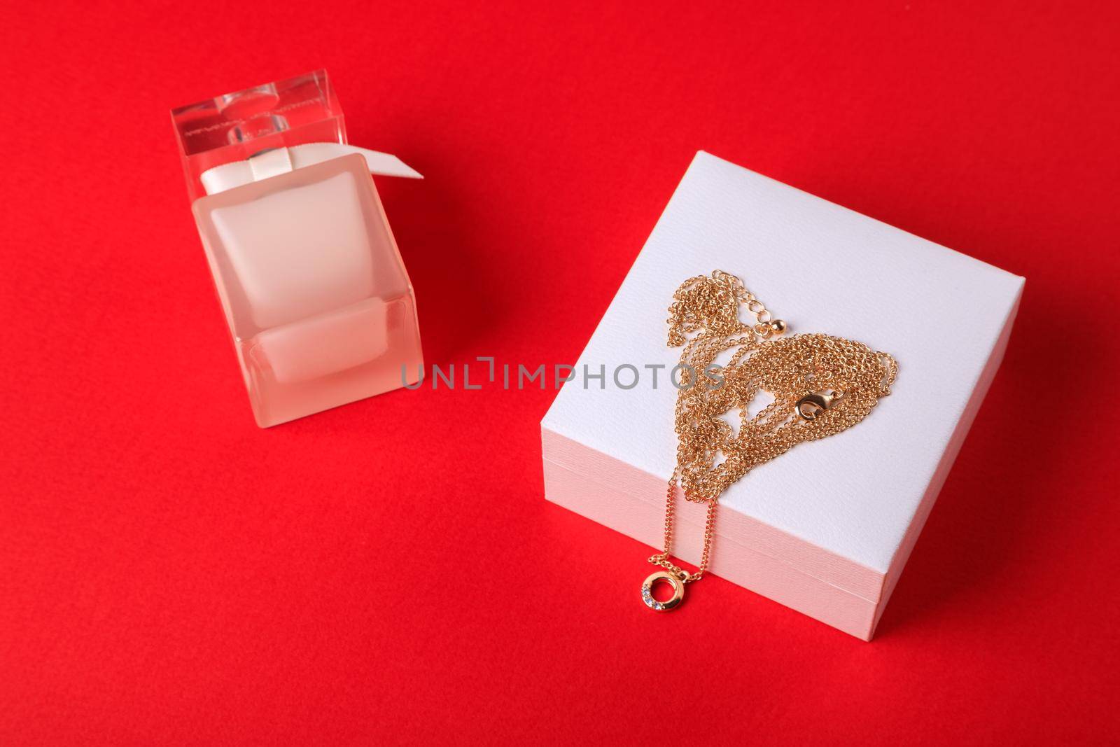 A gift for Valentine's Day. Perfume and a box with a gold chain on a red background.