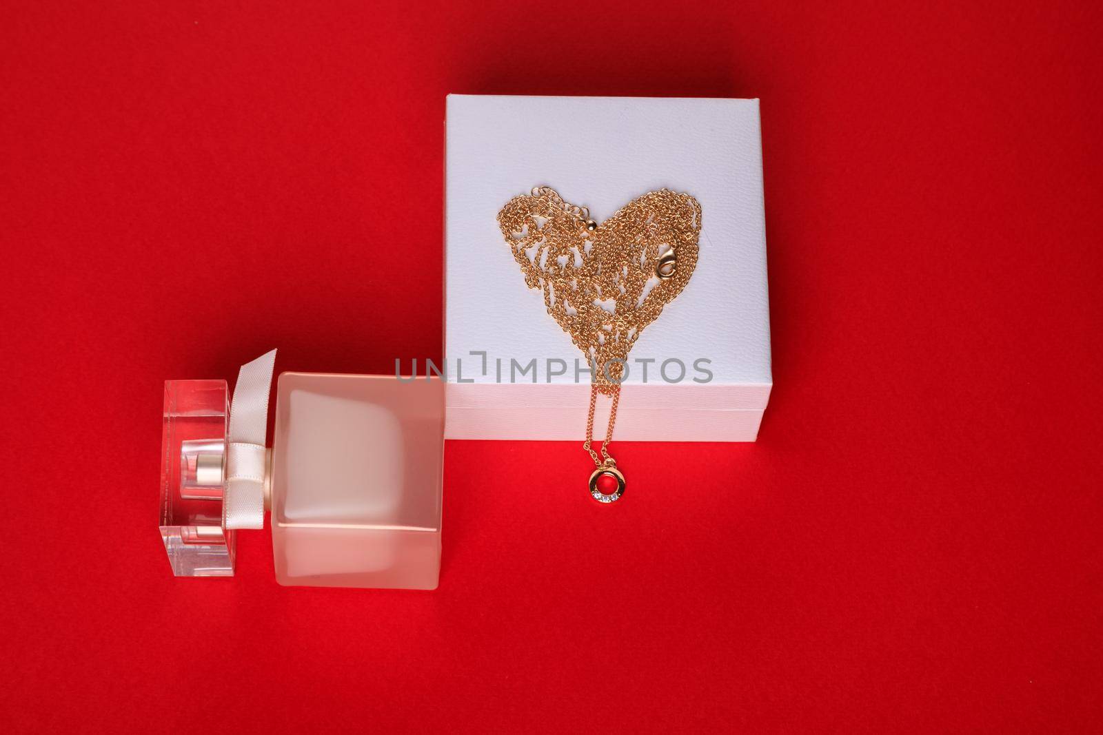 A gift for Valentine's Day. Perfume and a box with a gold chain on a red background.
