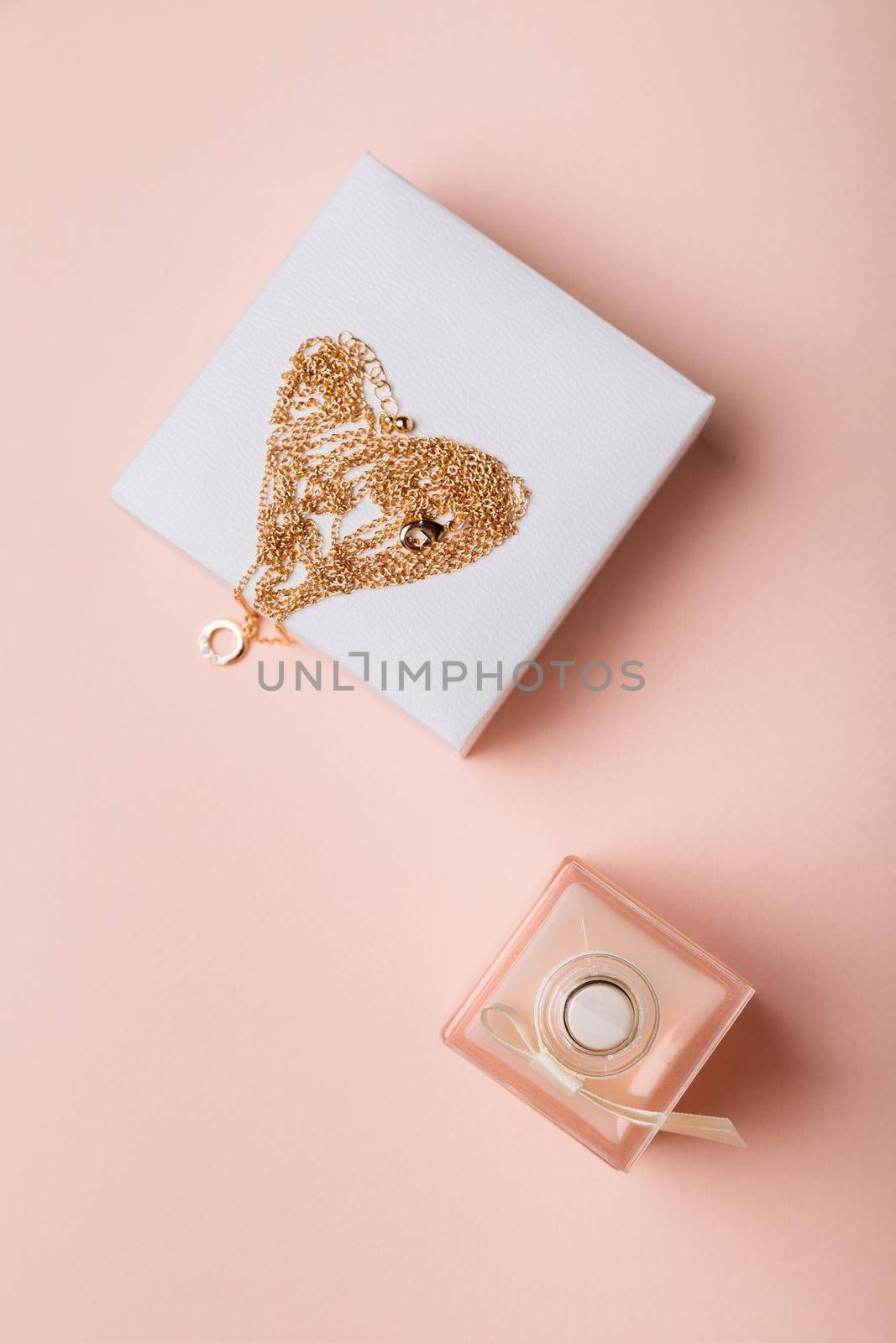 A gift for Valentine's Day. Perfume and a box with a gold chain on a pink background.
