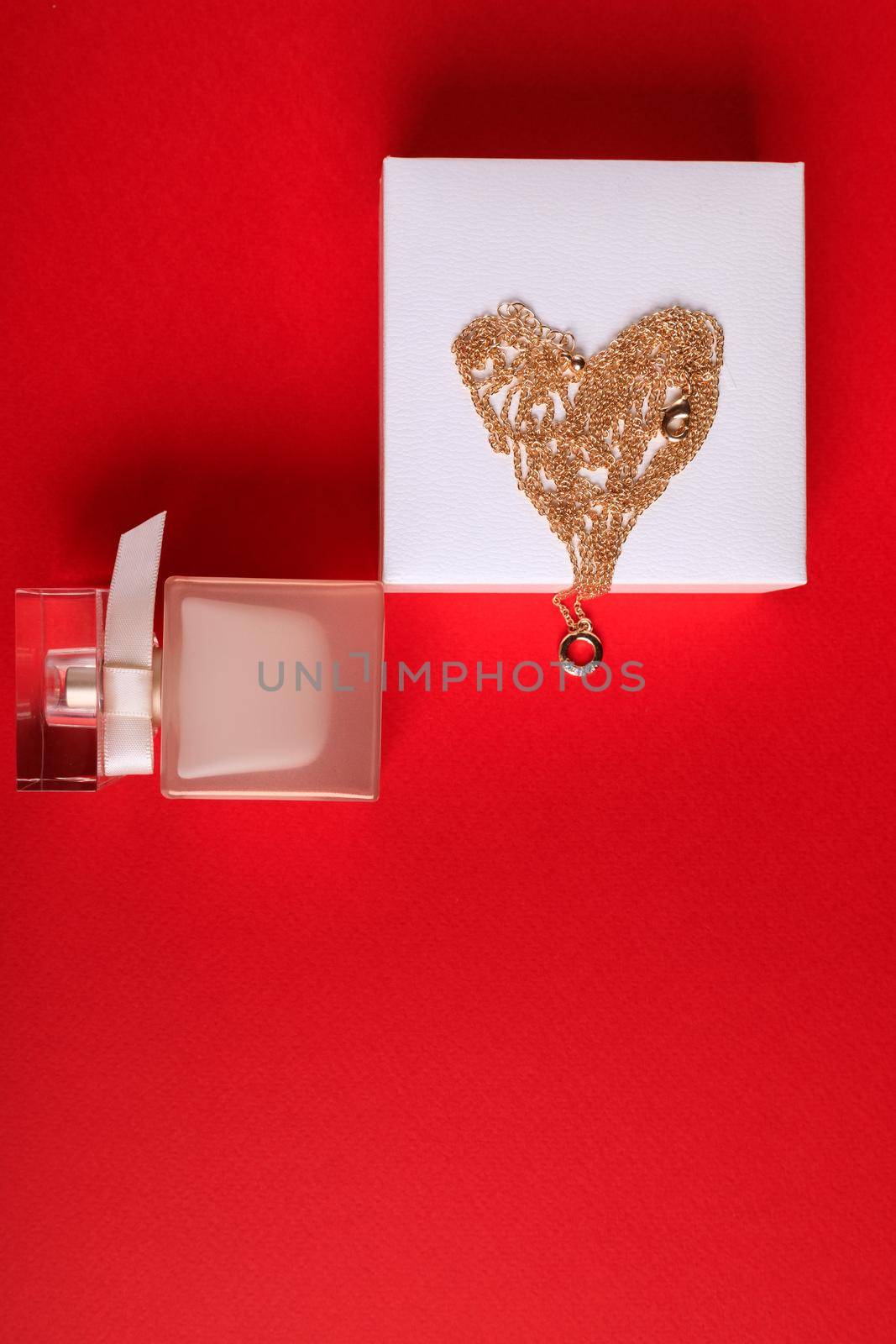 A gift for Valentine's Day. Perfume and a box with a gold chain on a red background.