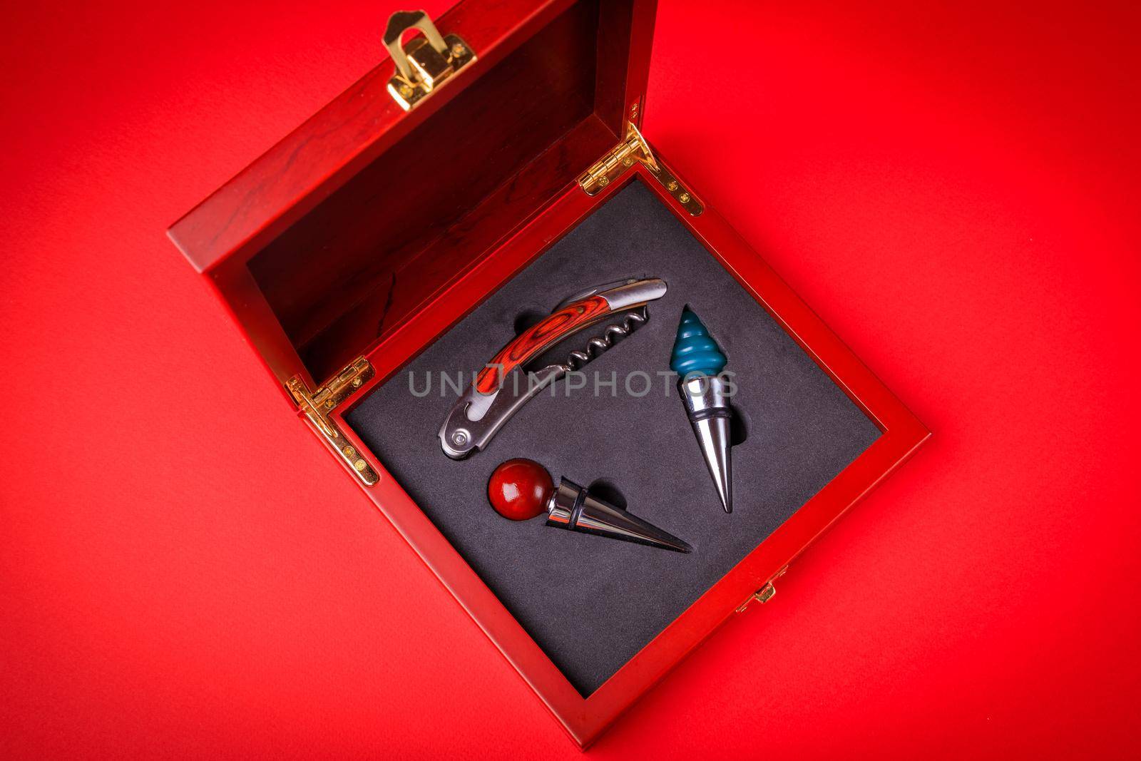 Gift set of corkscrew and removable lids. Wine corks and bottle openers in a wooden box on a red background.