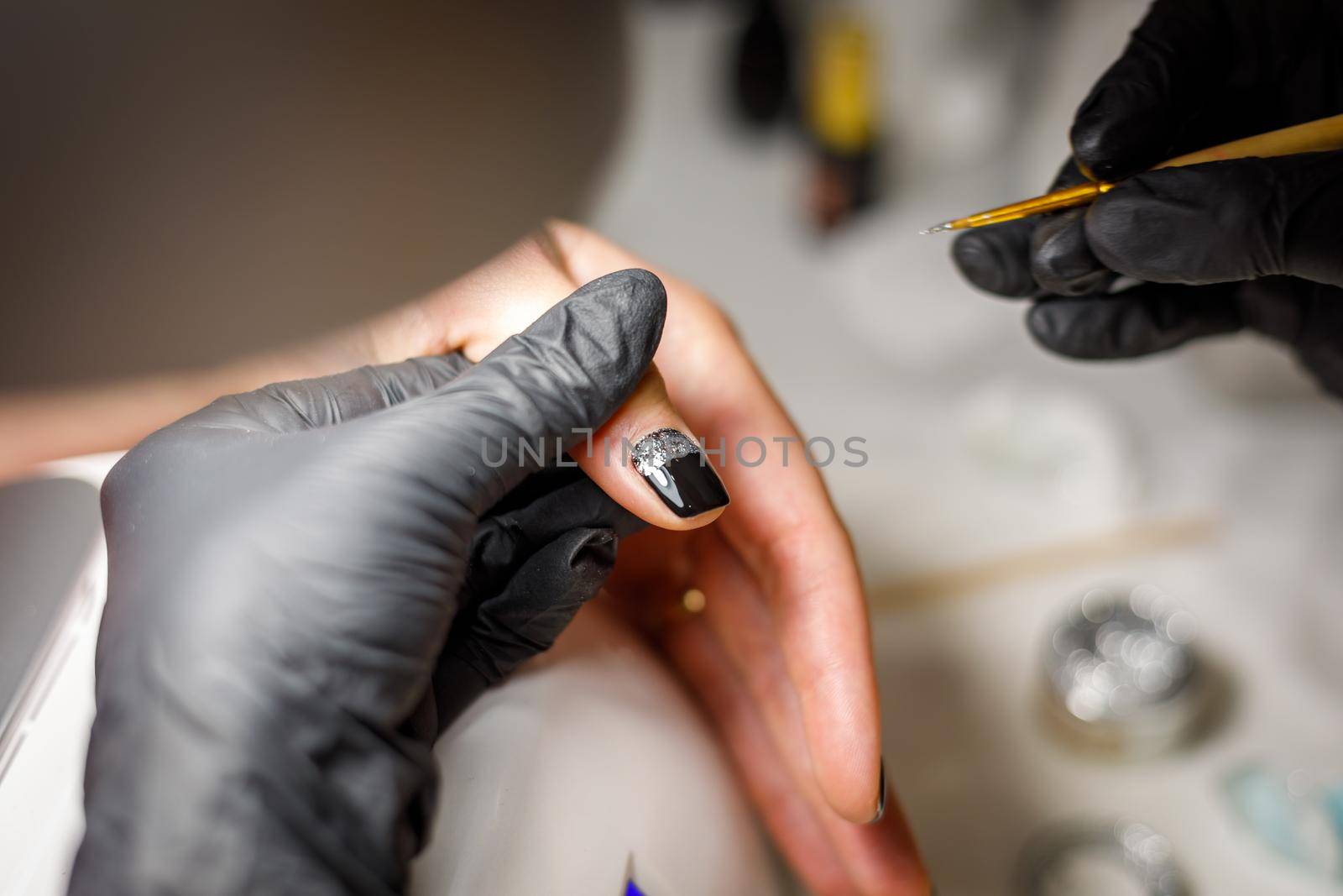 In a beauty salon, the master does a manicure, applies a pattern to the nail with a brush, black varnish with a golden pattern.