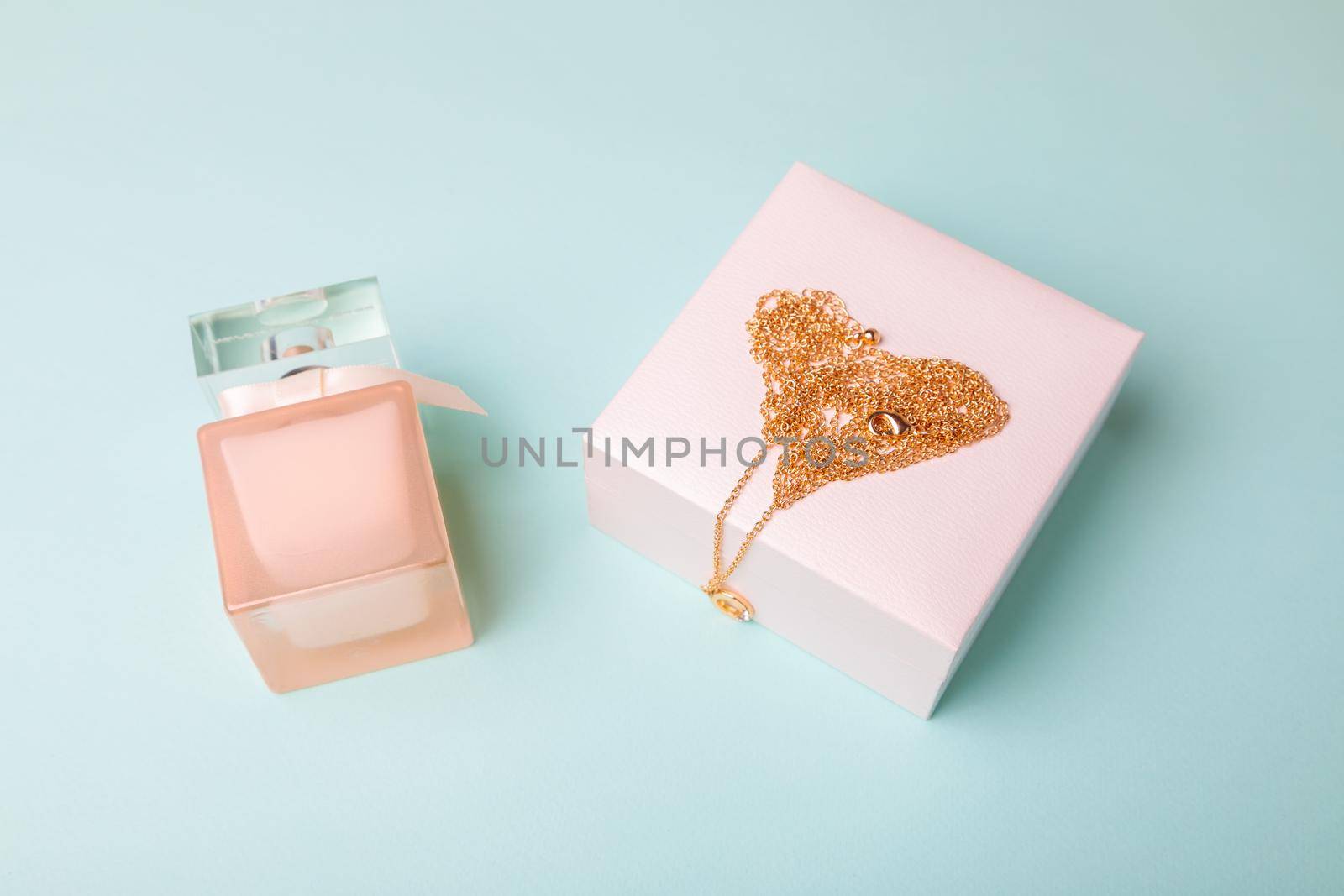 A gift for Valentine's Day. Perfume and a box with a gold chain on a blue background. Chain in the shape of a heart.