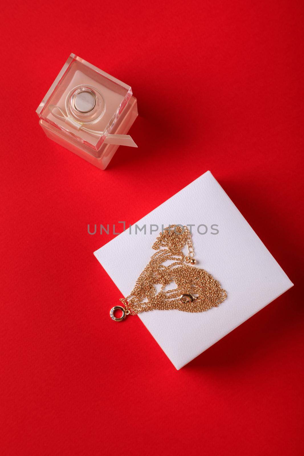 A gift for Valentine's Day. Perfume and a box with a gold chain on a red background.