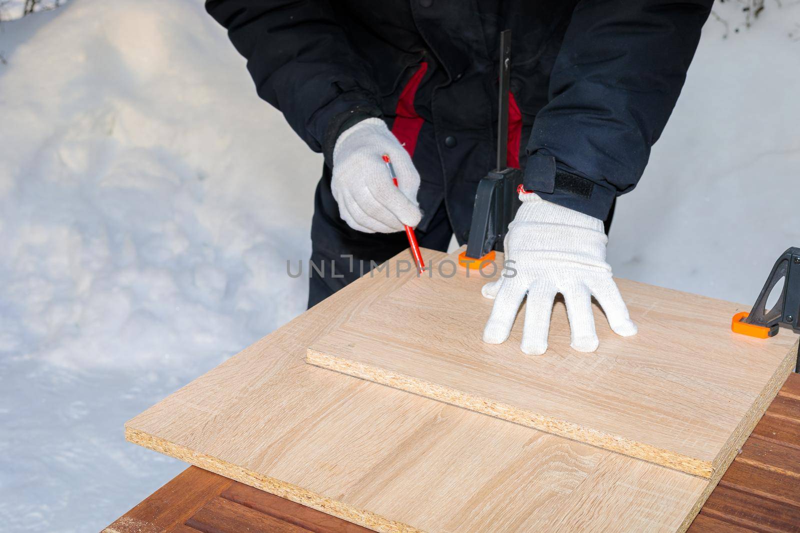 A man, a worker, marks it with a square and a pencil on a chipboard board. Draws a line.