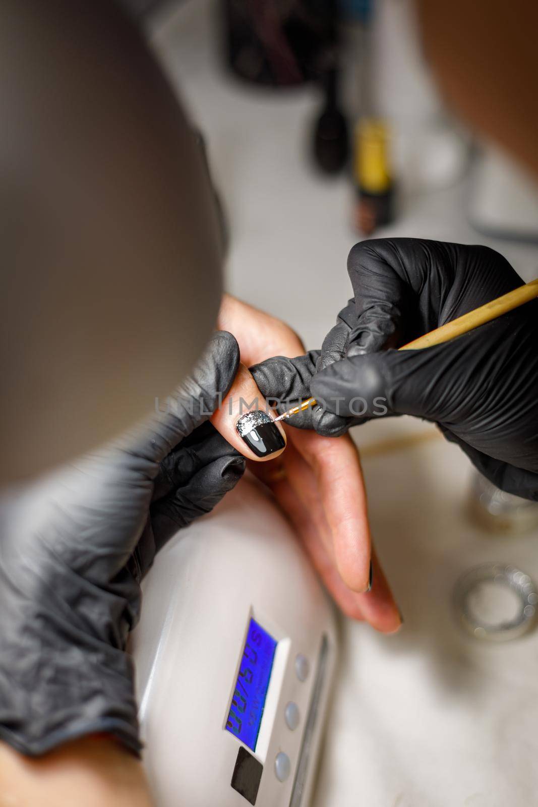 In a beauty salon, the master does a manicure, applies a pattern to the nail with a brush, black varnish with a golden pattern.