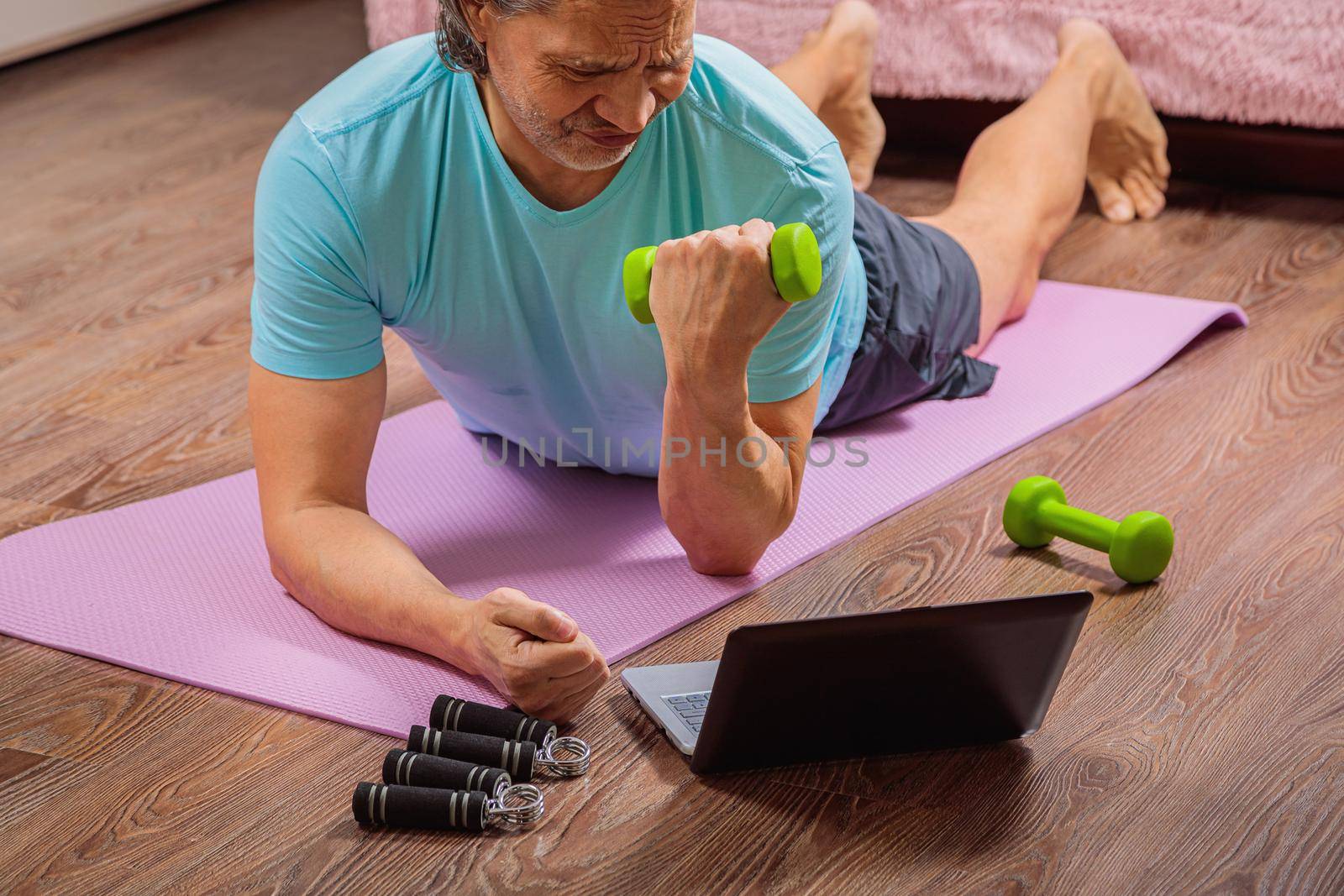 50 year old man performs exercises lying on mat at home looking at computer by Yurich32