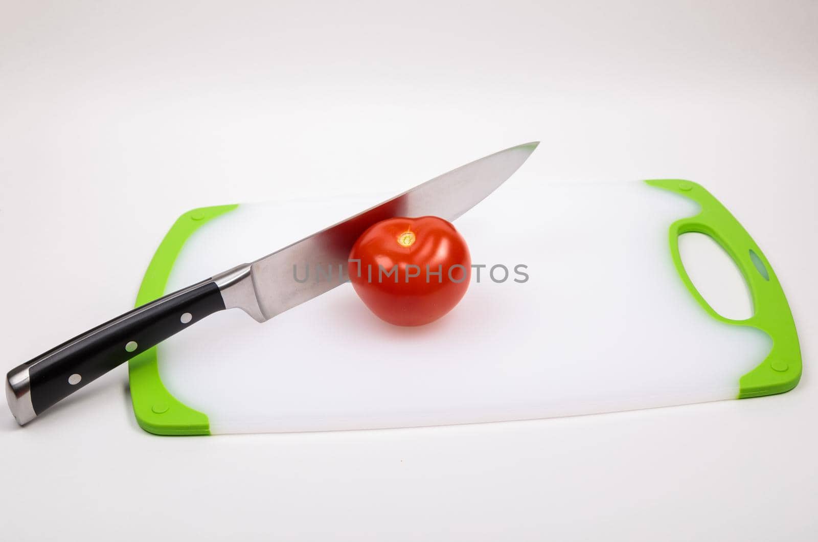 A fresh red tomato and a large chef's knife lie on a cutting board. On an isolated white background.