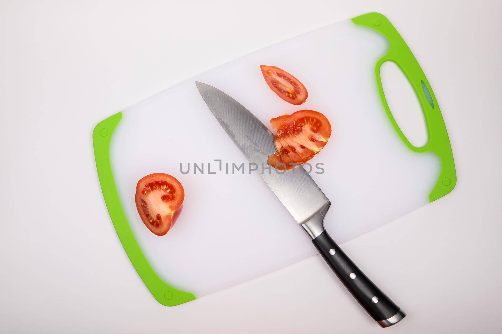 On a cutting board is a fresh red cut tomato and a large chef's knife. On an isolated white background.