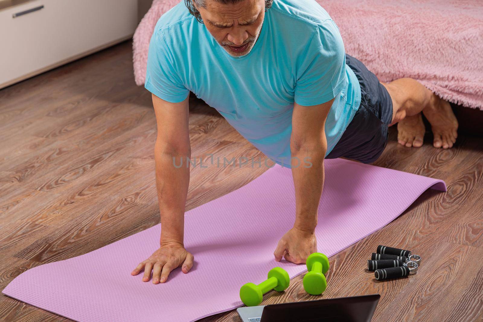 50 year old man performs exercises lying on mat at home looking at computer by Yurich32