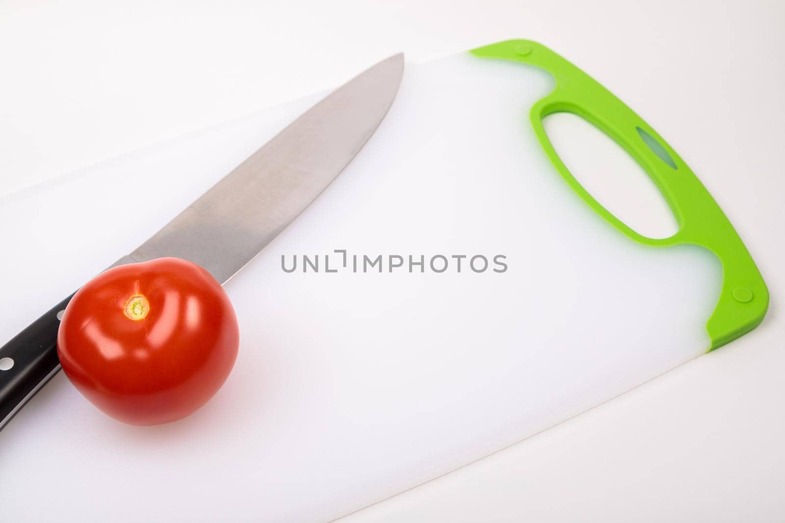 A fresh red tomato and a large chef's knife lie on a cutting board. On an isolated white background.