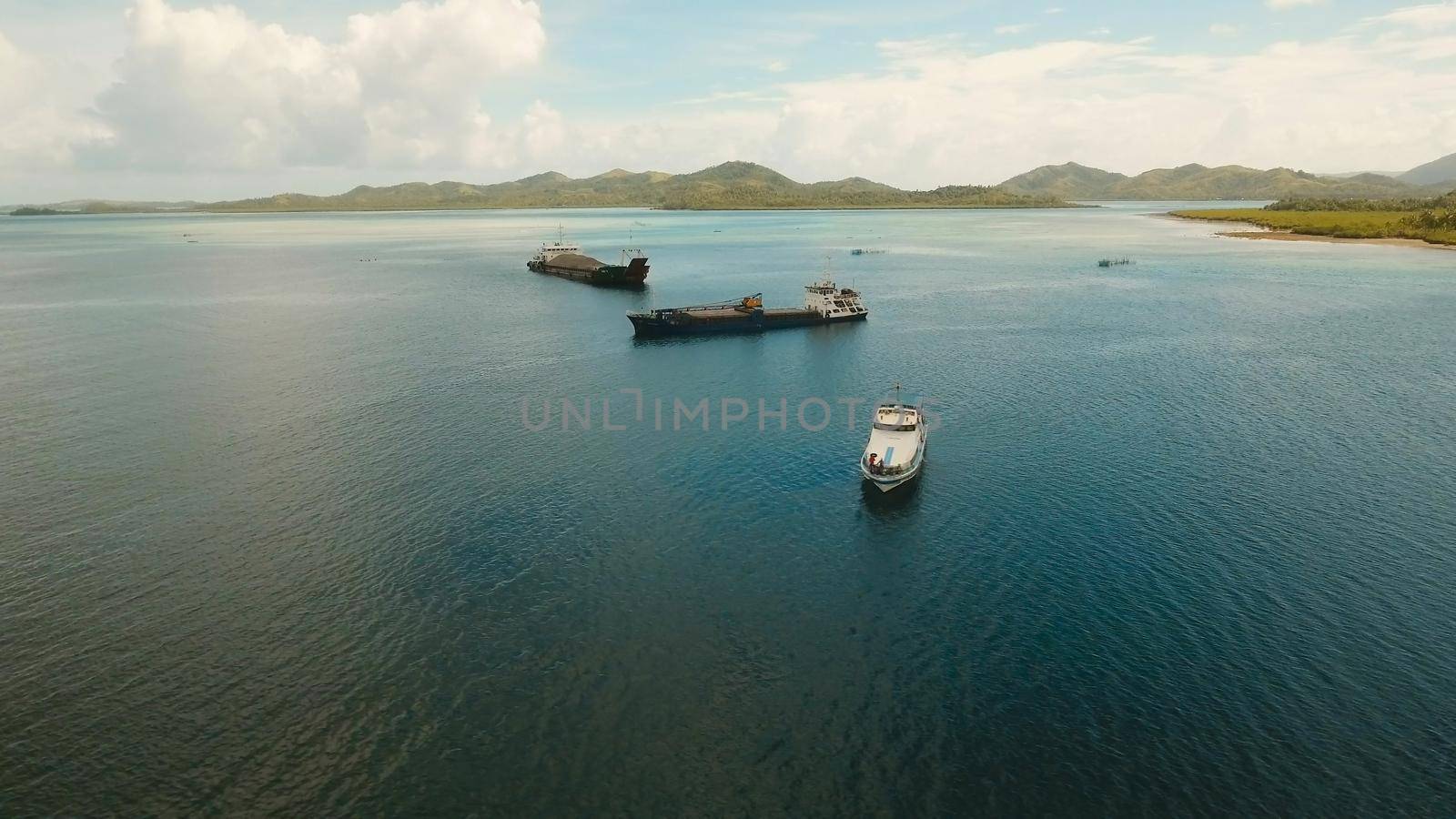 Aerial view Cargo and passenger ships in a beautiful lagoon on Siargao. Flying over the water surface of the sea with ships, blue sky and clouds.