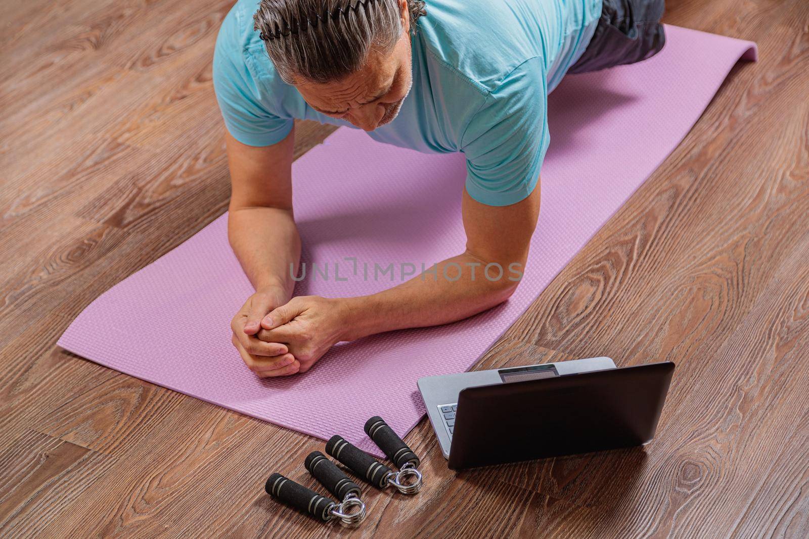 50 year old man performs exercises lying on mat at home looking at computer by Yurich32