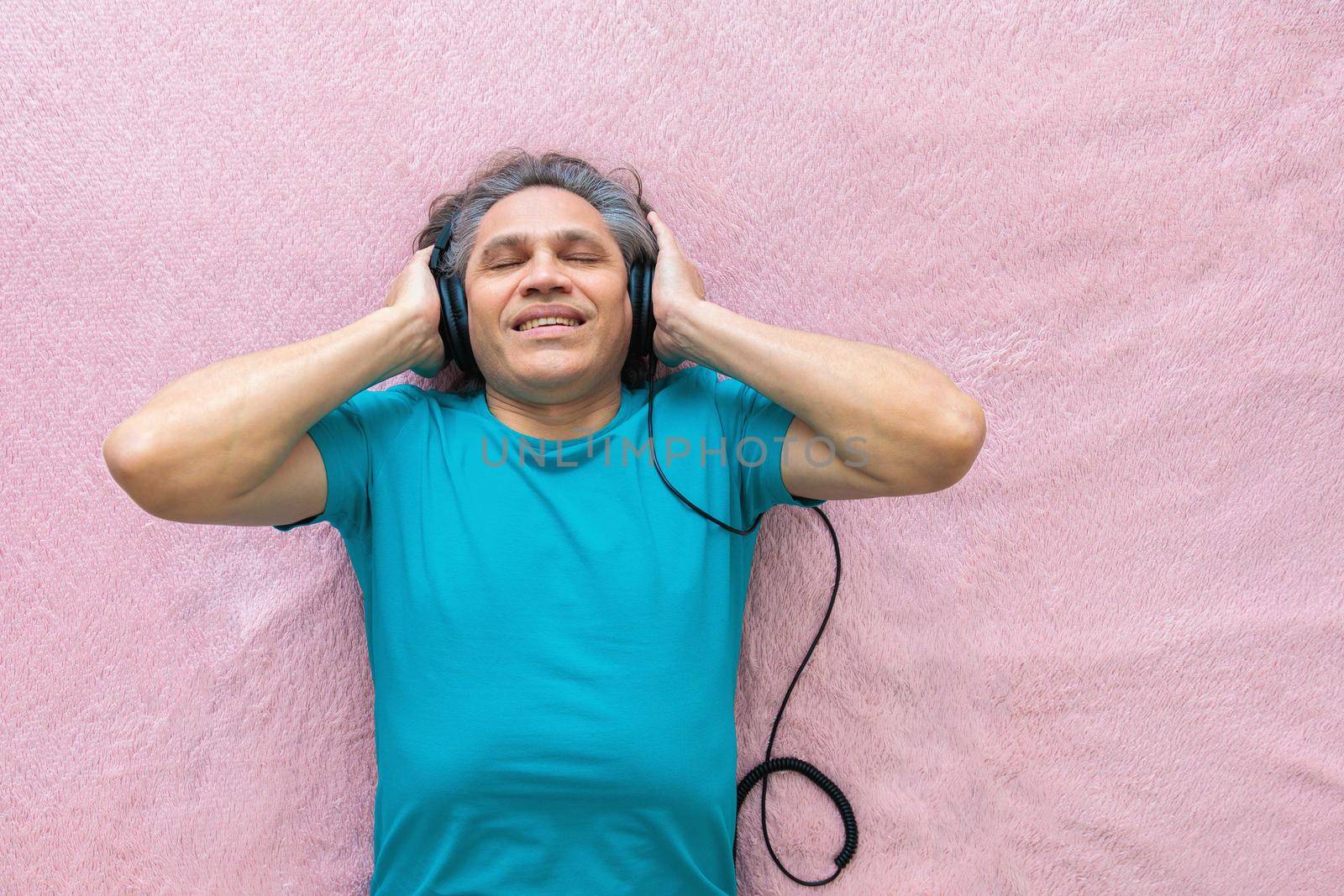 50-year-old man listens to music with headphones at home, lying on the bed. Relaxing, enjoying.