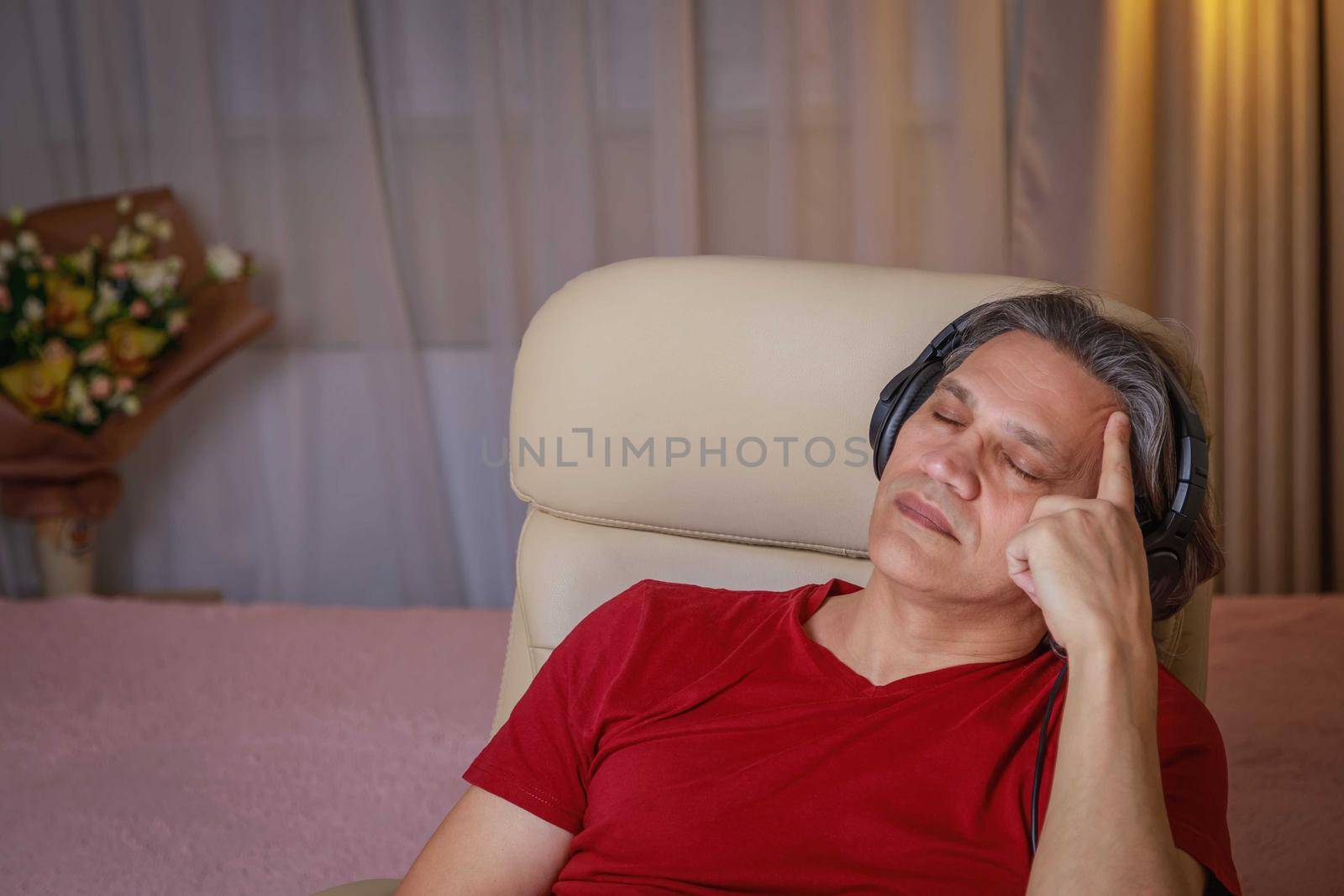 50-year-old man listens to music on headphones at home, sitting in a chair. Relaxing delight.