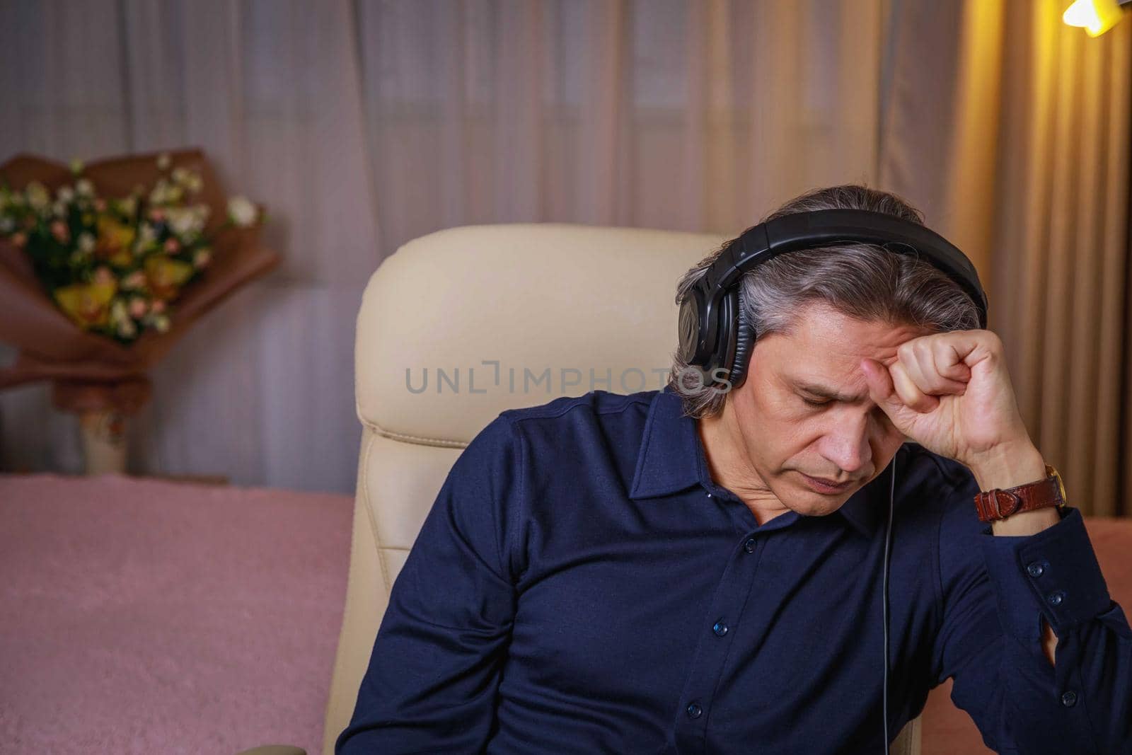 50-year-old man listens to music on headphones at home, sitting in a chair. Relaxing delight.