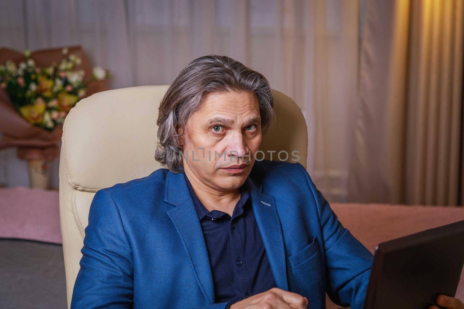 A 50-year-old man with long gray hair works at a computer. Works at home, remotely.