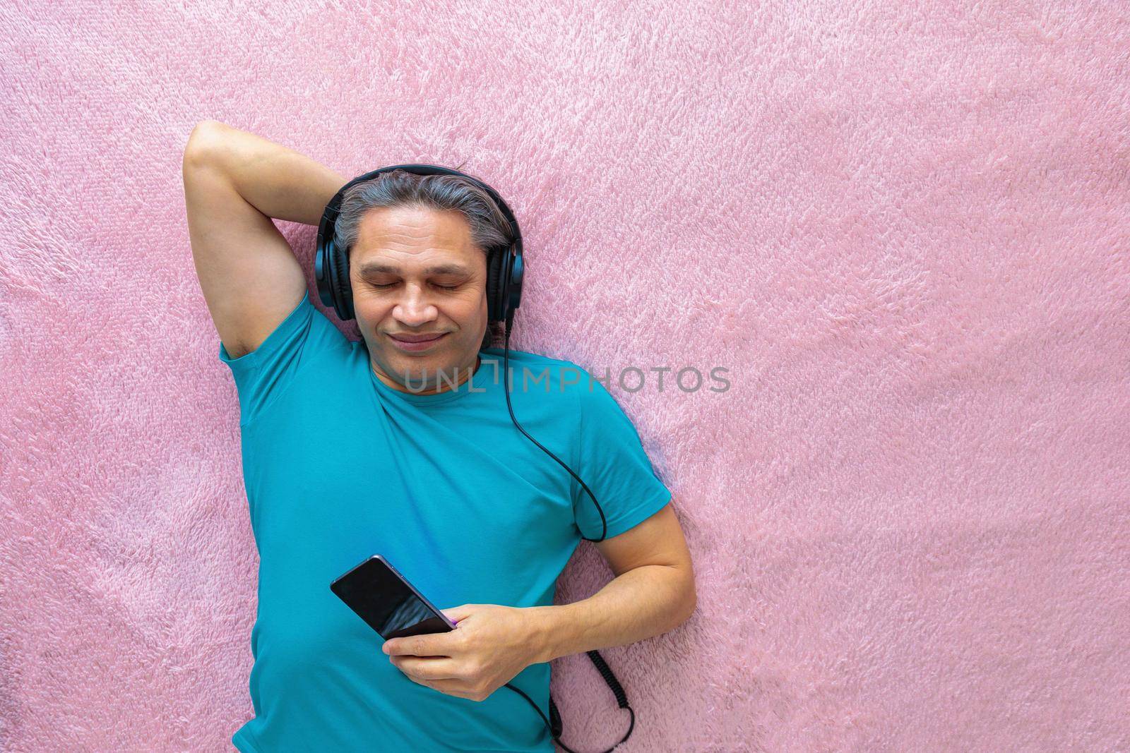 50-year-old man listens to music with headphones at home, lying on the bed. Relaxing, enjoying.