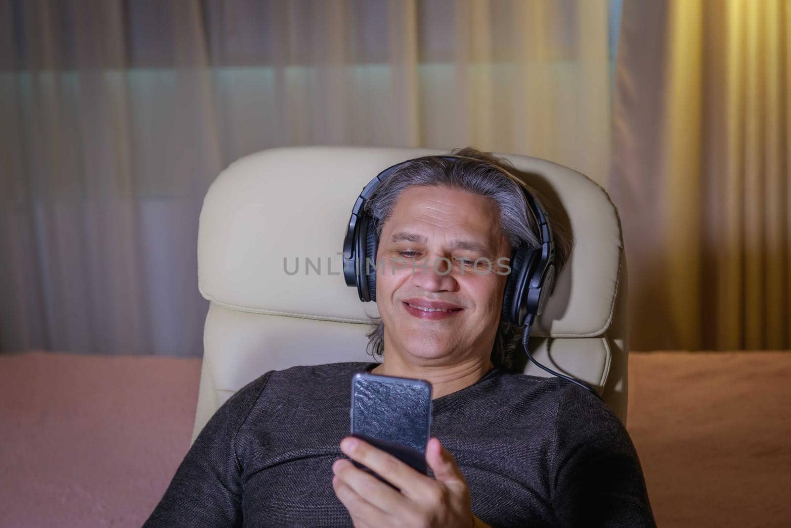 50-year-old man listens to music on headphones at home, sitting in a chair. Relaxing delight.