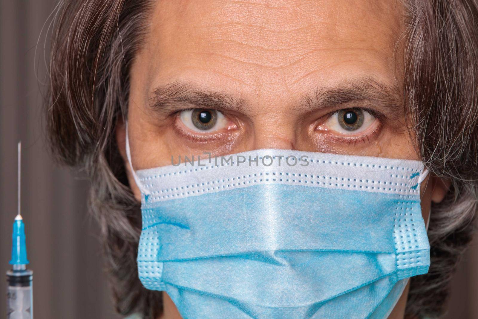 Adult man in a medical mask. Close-up eyes. Syringe in hand. Health safety concept