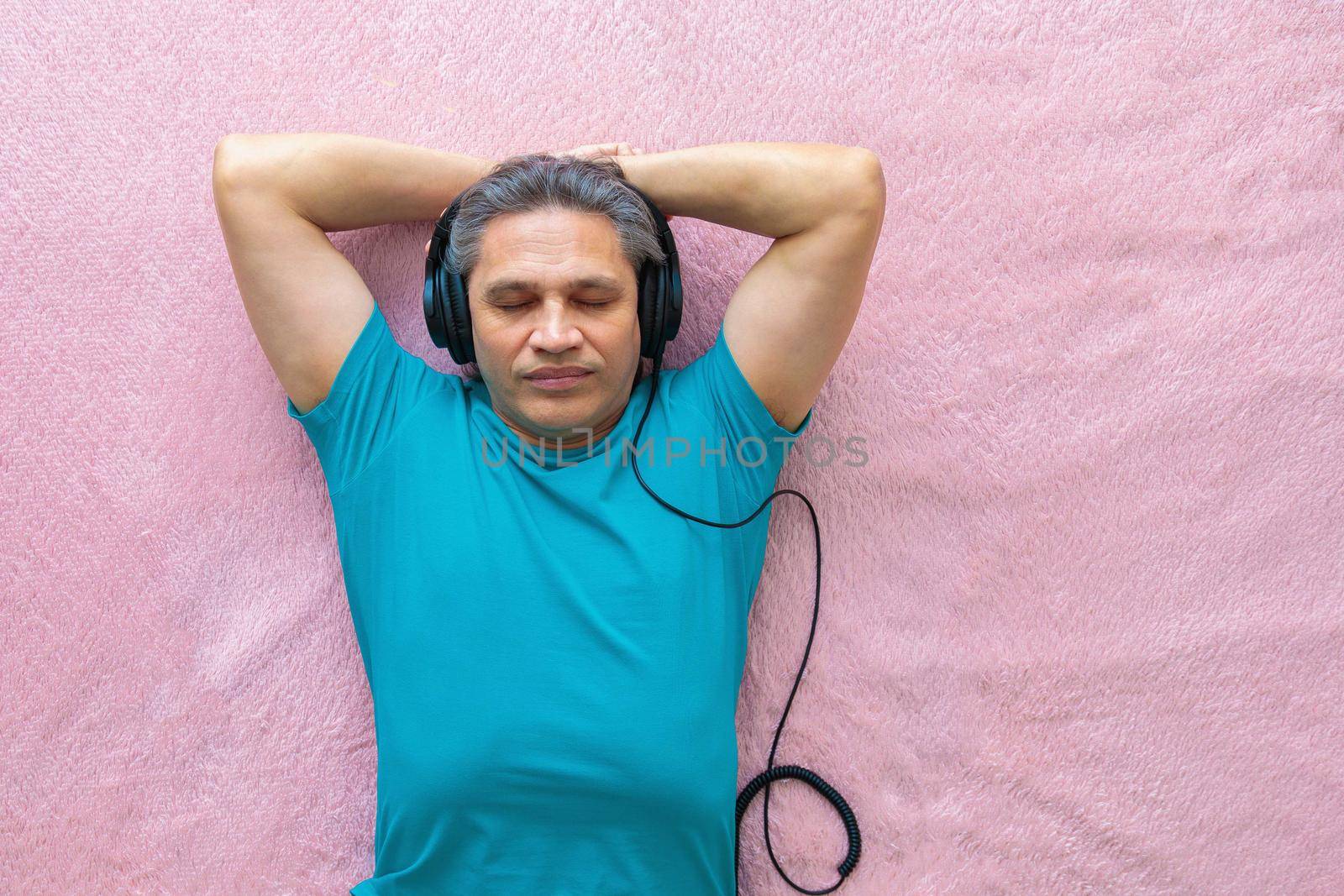 50-year-old man listens to music with headphones at home, lying on the bed. Relaxing, enjoying.