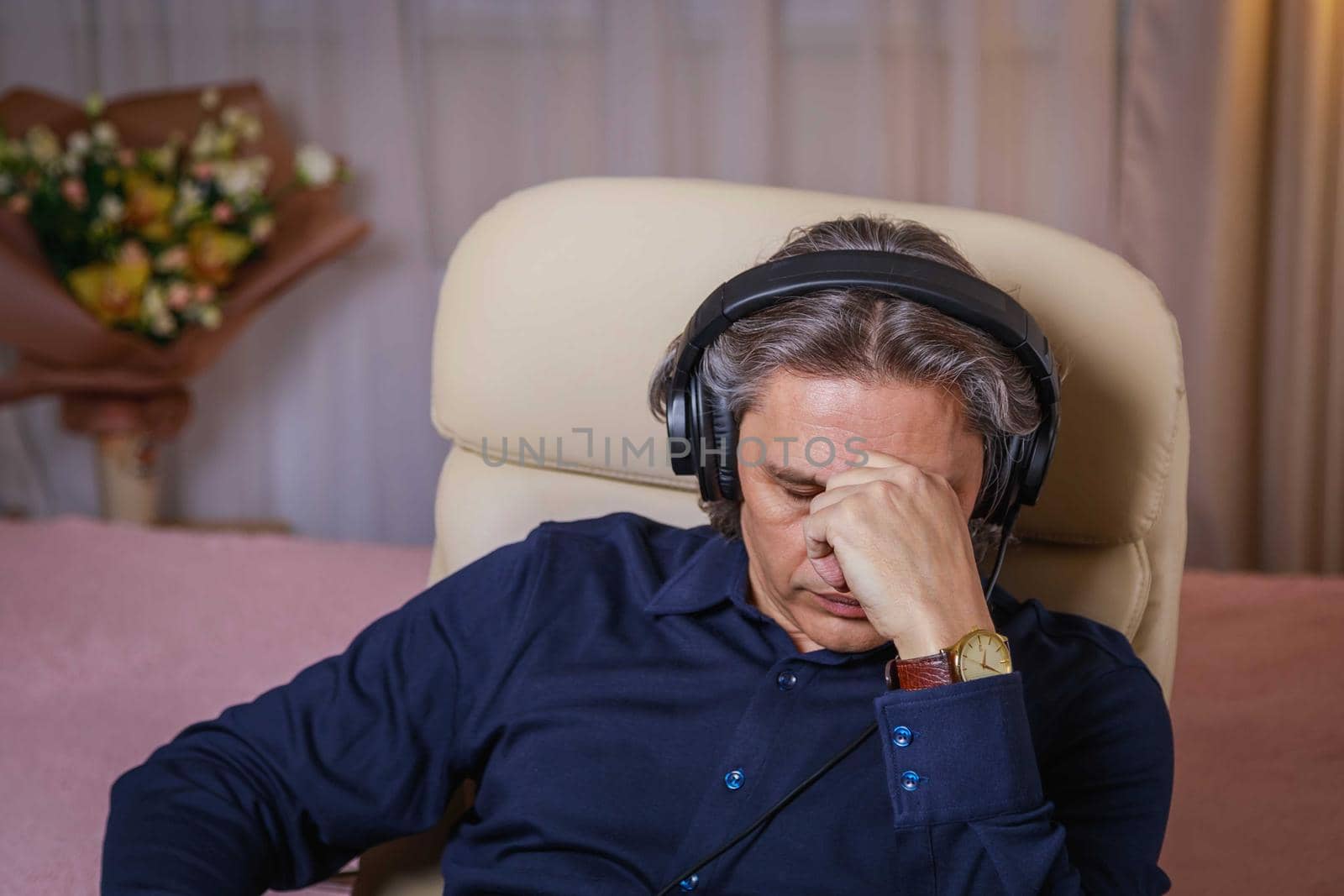 50-year-old man listens to music on headphones at home, sitting in a chair. by Yurich32