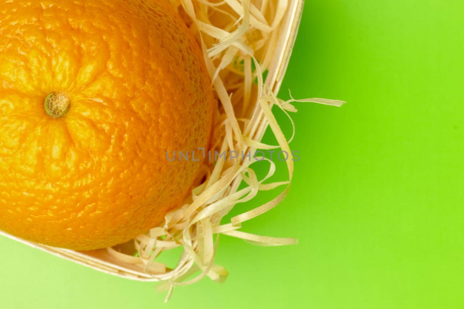 orange in a basket with shavings on a green background. High quality photo