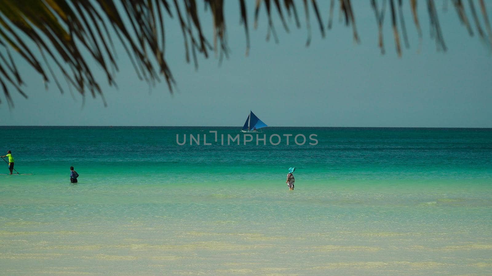Tourists on a sandy beach and blue sea through palm branches. Summer and travel vacation concept. Boracay, Philippines