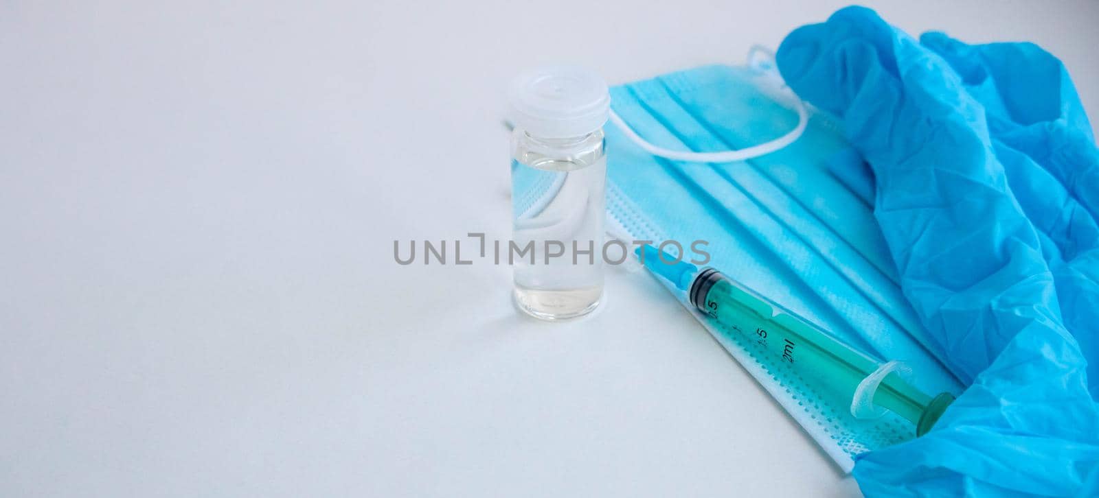 A syringe, gloves, mask, and a bottle of vaccine stand on a blue background. For the prevention, immunization and treatment of coronavirus infection. The concept of medicine and health care.