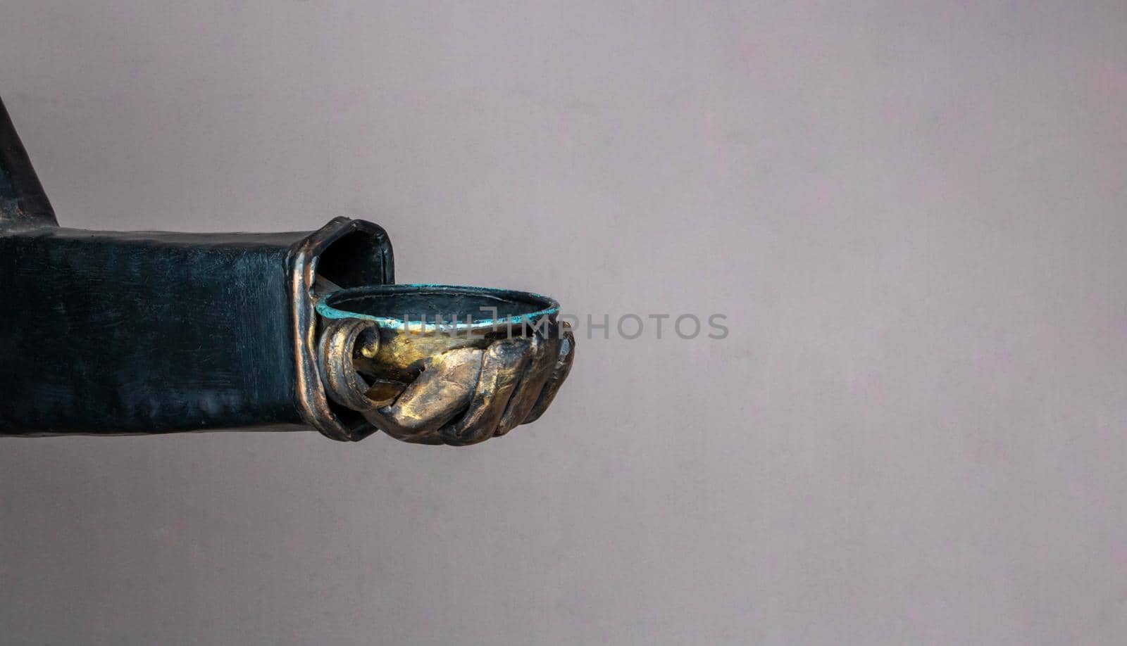 Copper hand with a cup on a beige background under the open sky.