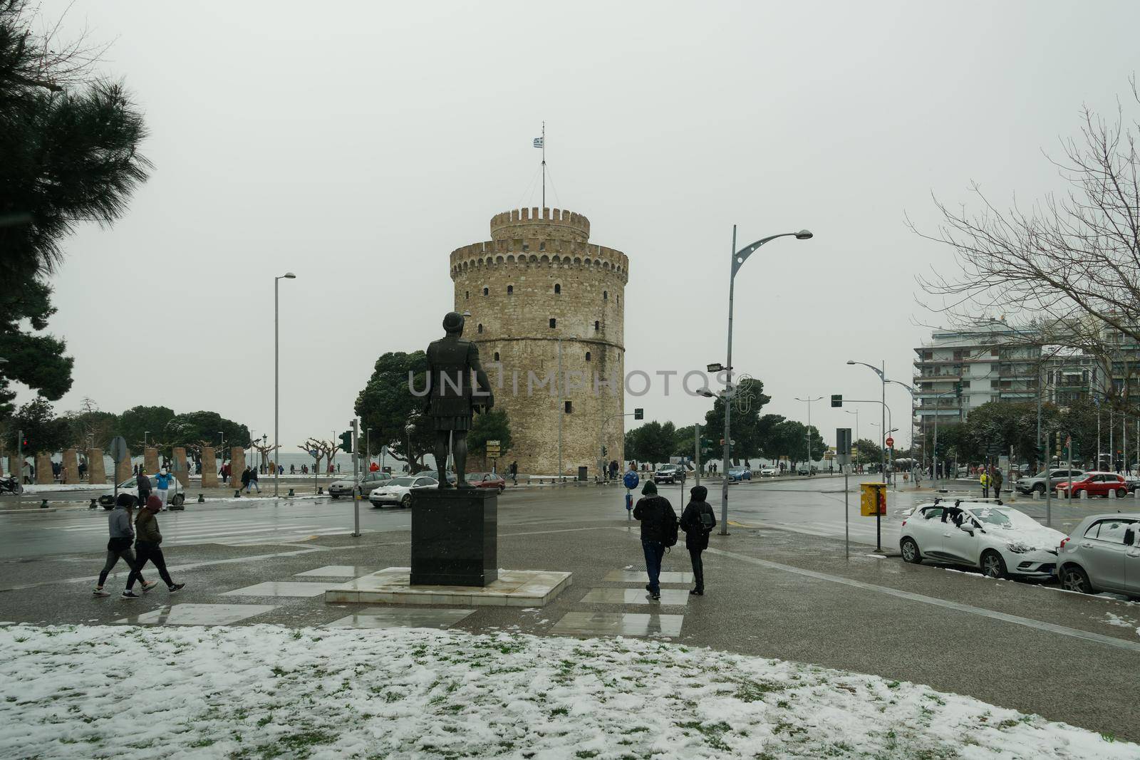 People in warm clothes and covid-19 masks around White Tower landmark with snow falling.