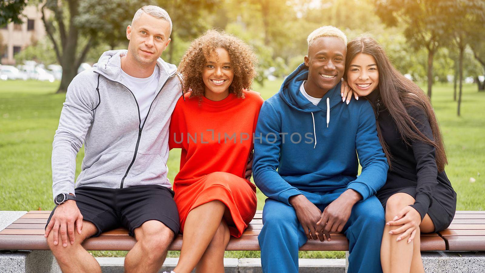 Multi-ethnic group teenage friends. African-american asian caucasian student spending time together Multiracial friendship Happy smiling People dressed colorful sportswear sitting bench park outdoor