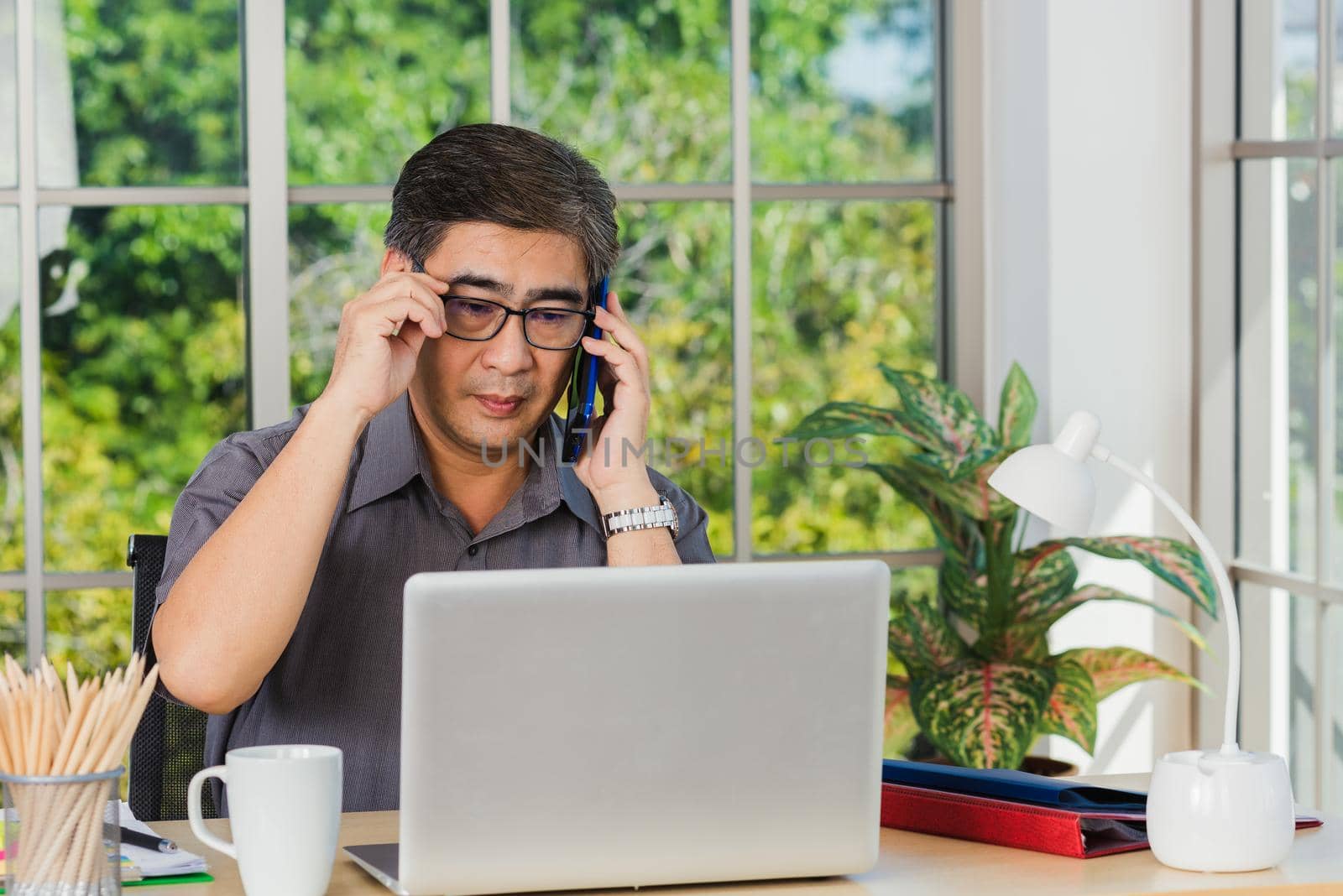 senior businessman sitting on desk office he using his mobile phone by Sorapop