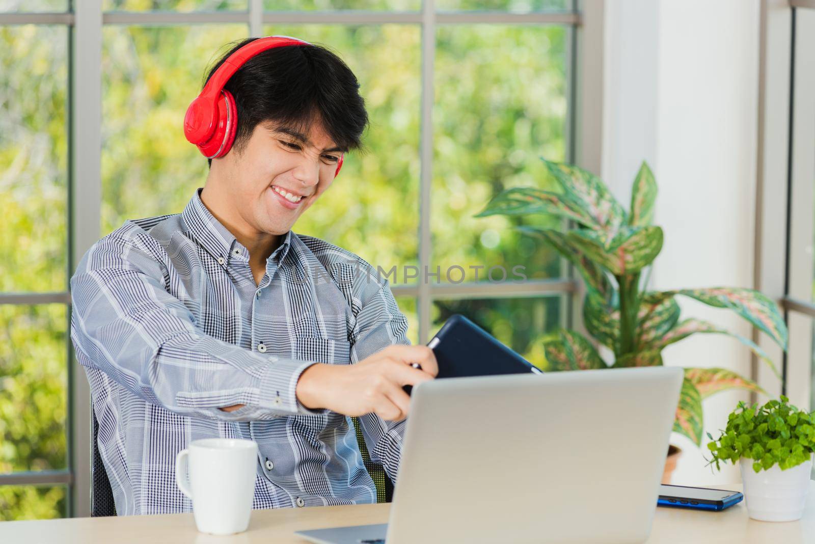 Asian young business man with red headphones he sitting on desk workplace using digital tablet play racing online video games, confident handsome man lifestyle he smiles and funny