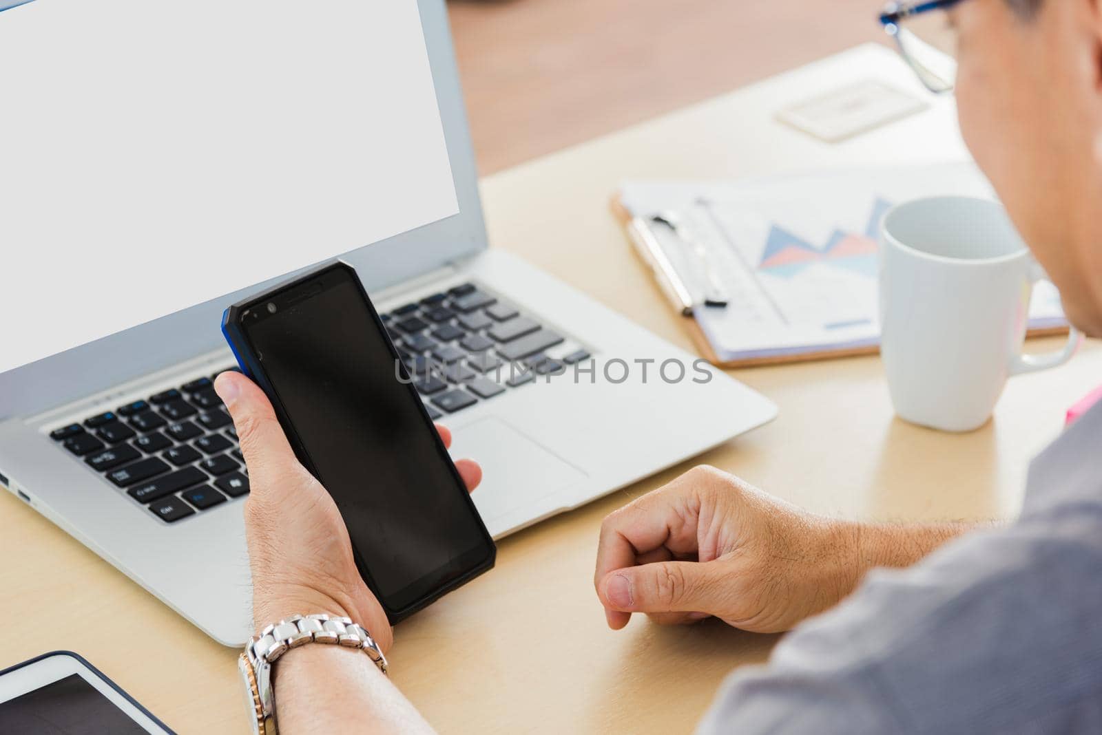 Old businessman using the mobile phone to video call conference on desk table at office. Asian senior business man working online on modern smartphone he looking at screen for remote online studying