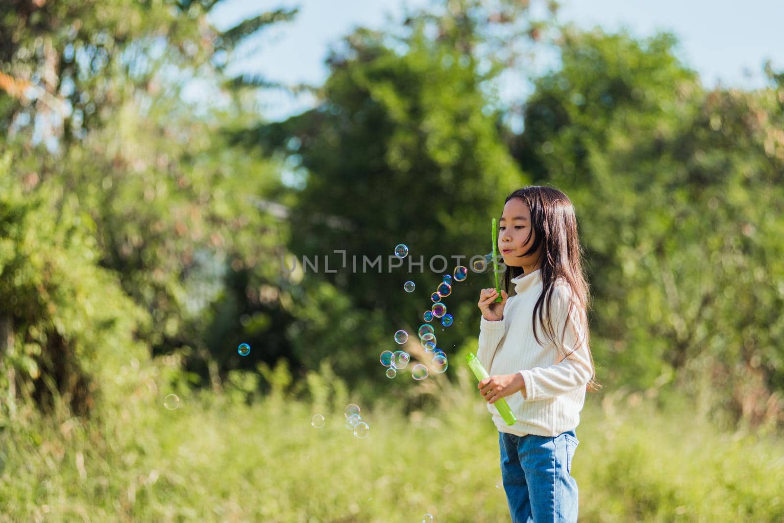 little cute girl child having fun and enjoying outdoor play blowing soap bubbles by Sorapop