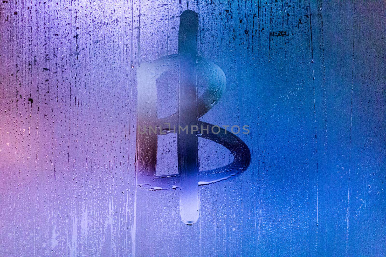 bitcoin symbol - handwritten on wet glass of night window, close-up with selective focus and background blur