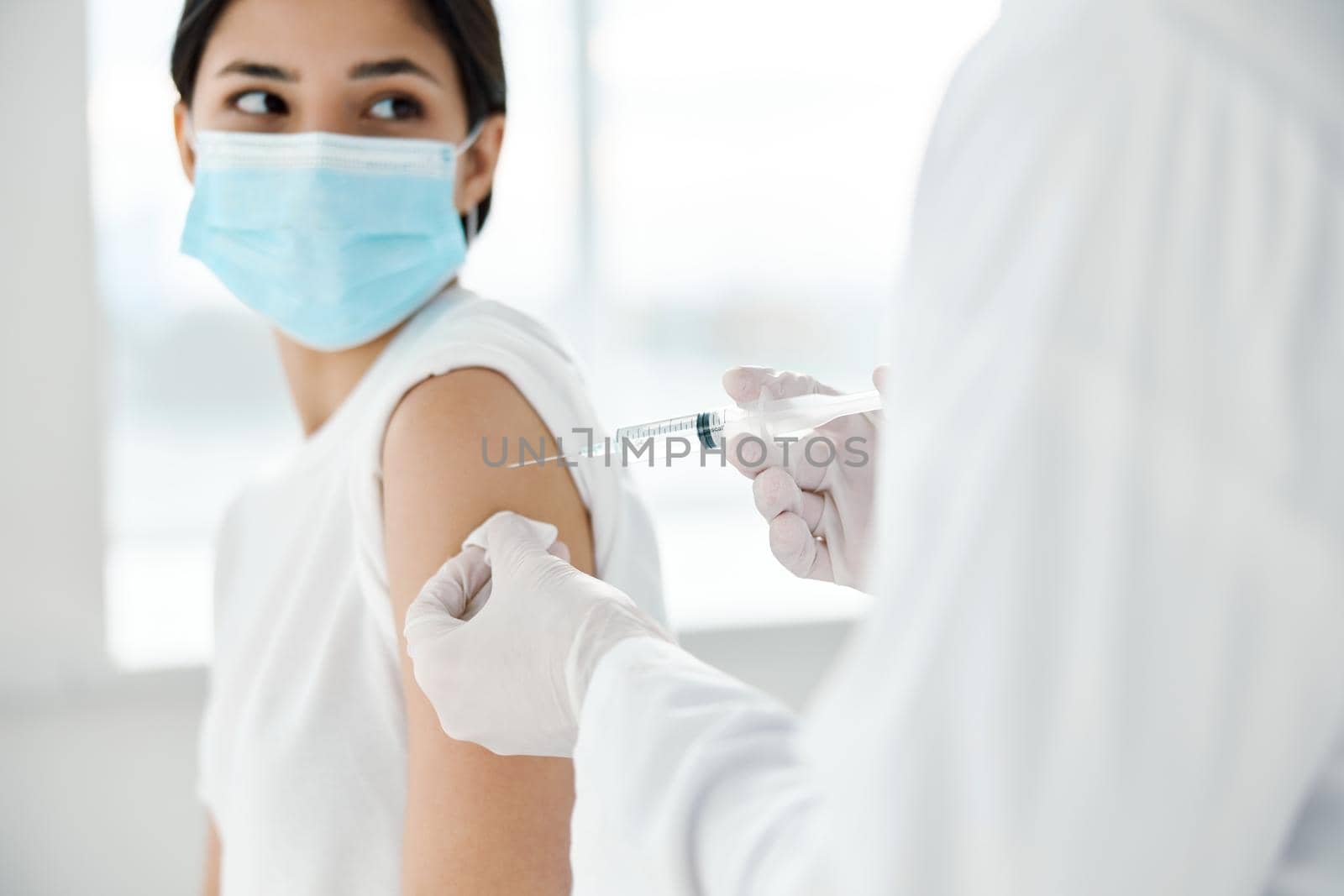 doctor in protective gloves makes an injection in the shoulder of a beautiful woman in a medical mask covid by SHOTPRIME