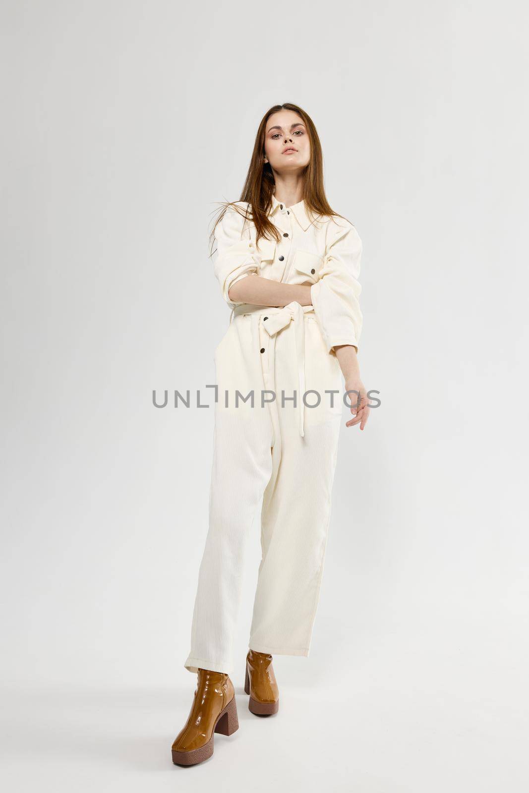 Woman in white jumpsuit brown boots in full growth isolated background by SHOTPRIME