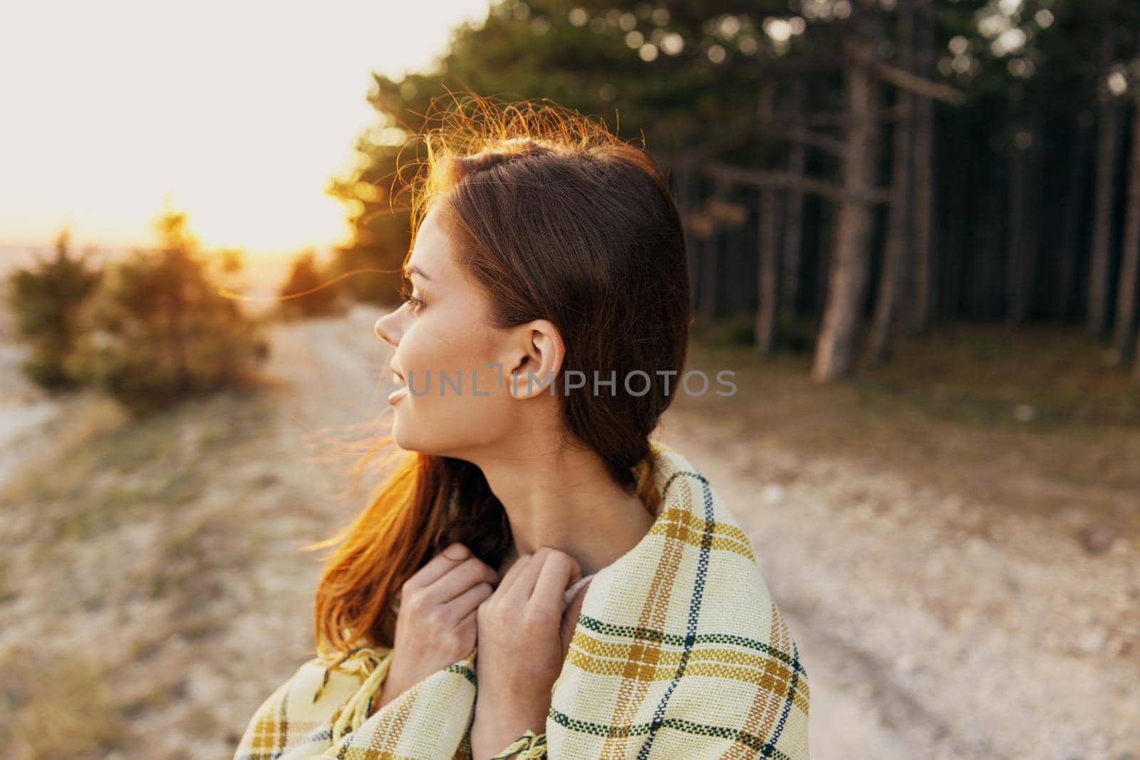 A woman at sunset on a path in the forest looks to the side and a plaid on her shoulders by SHOTPRIME